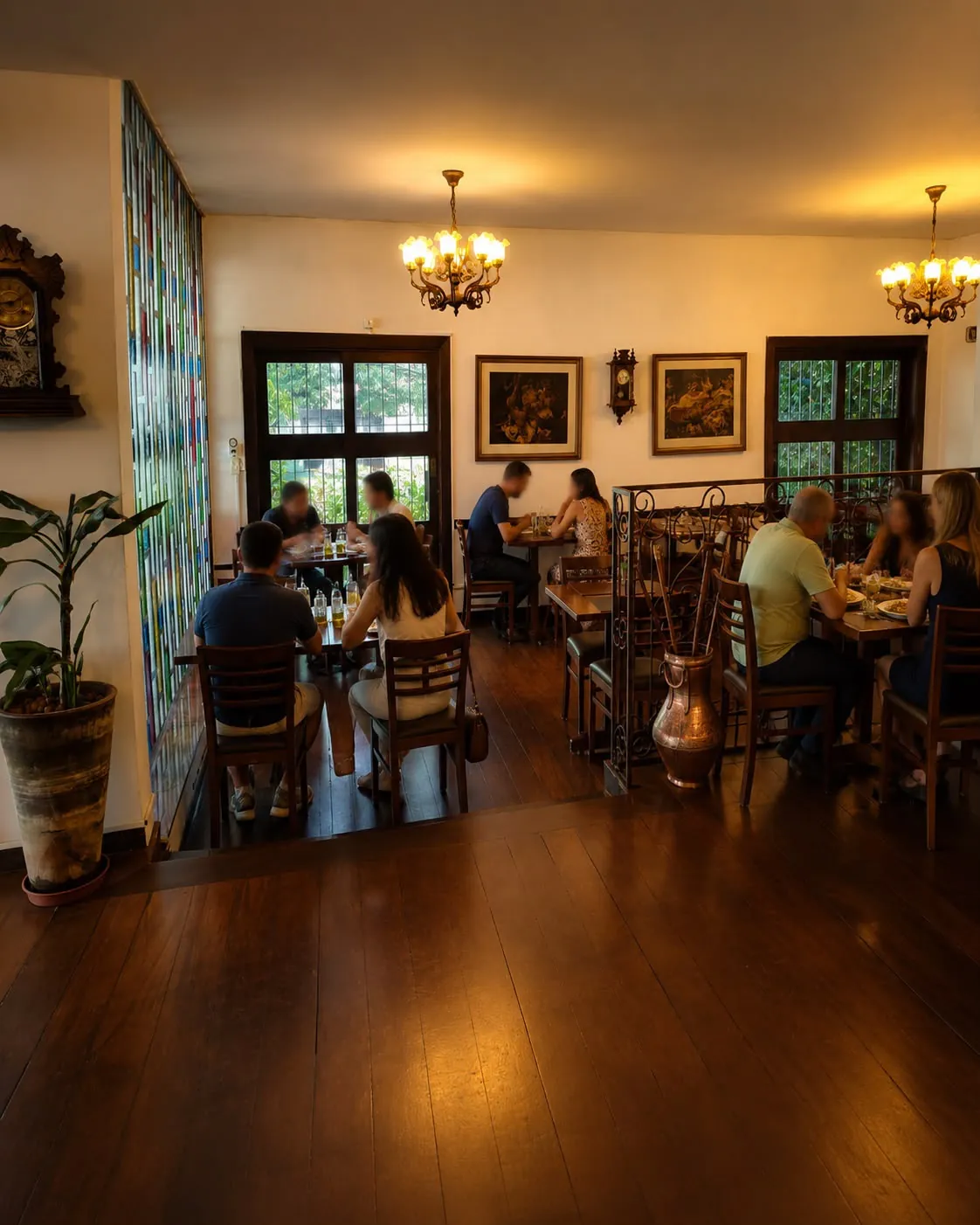 Salão do Empório Araçá com lustres acesos, vitral colorido e clientes almoçando